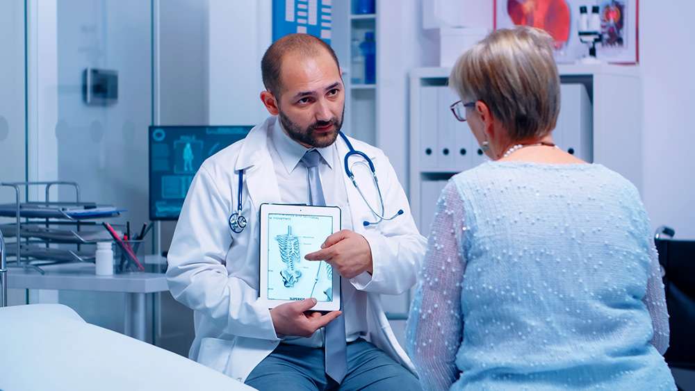 A photo of a physician and his patient looking at a tablet with a photo of the human skeletal system on it for the Bay area Endocronology website.