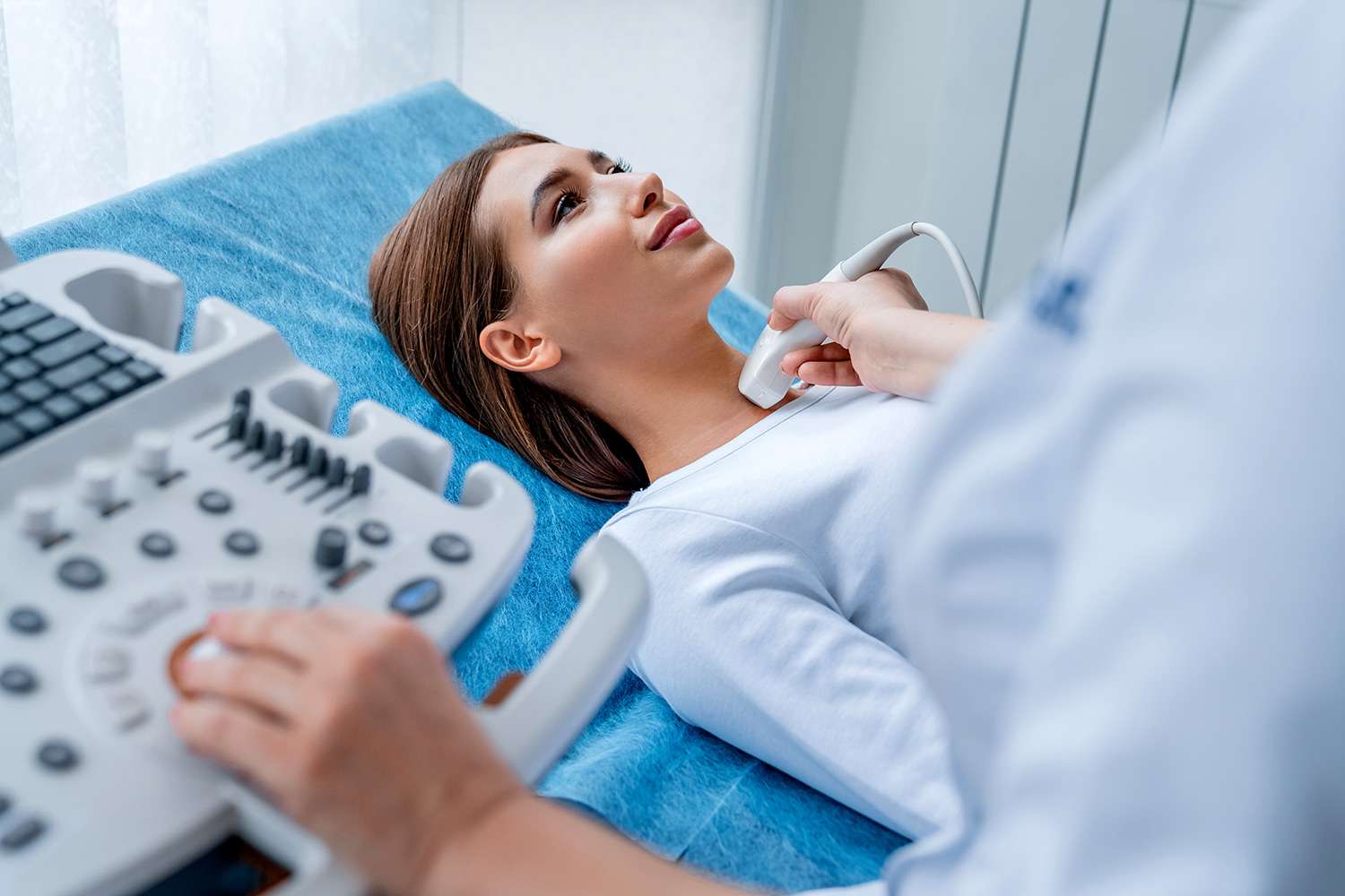 A photo of a female, with a medical practitioner holding an ultrasound device examining her lower neck for a blog post about Thyroid Disorders