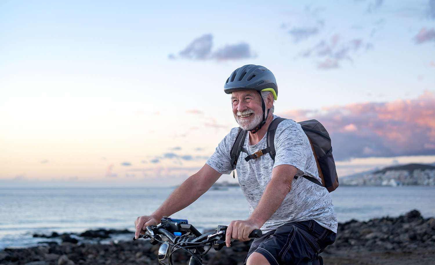 A photo of a senior man riding a bike, smiling, with the ocean in the background for a blog post that discusses pituitary disorders.