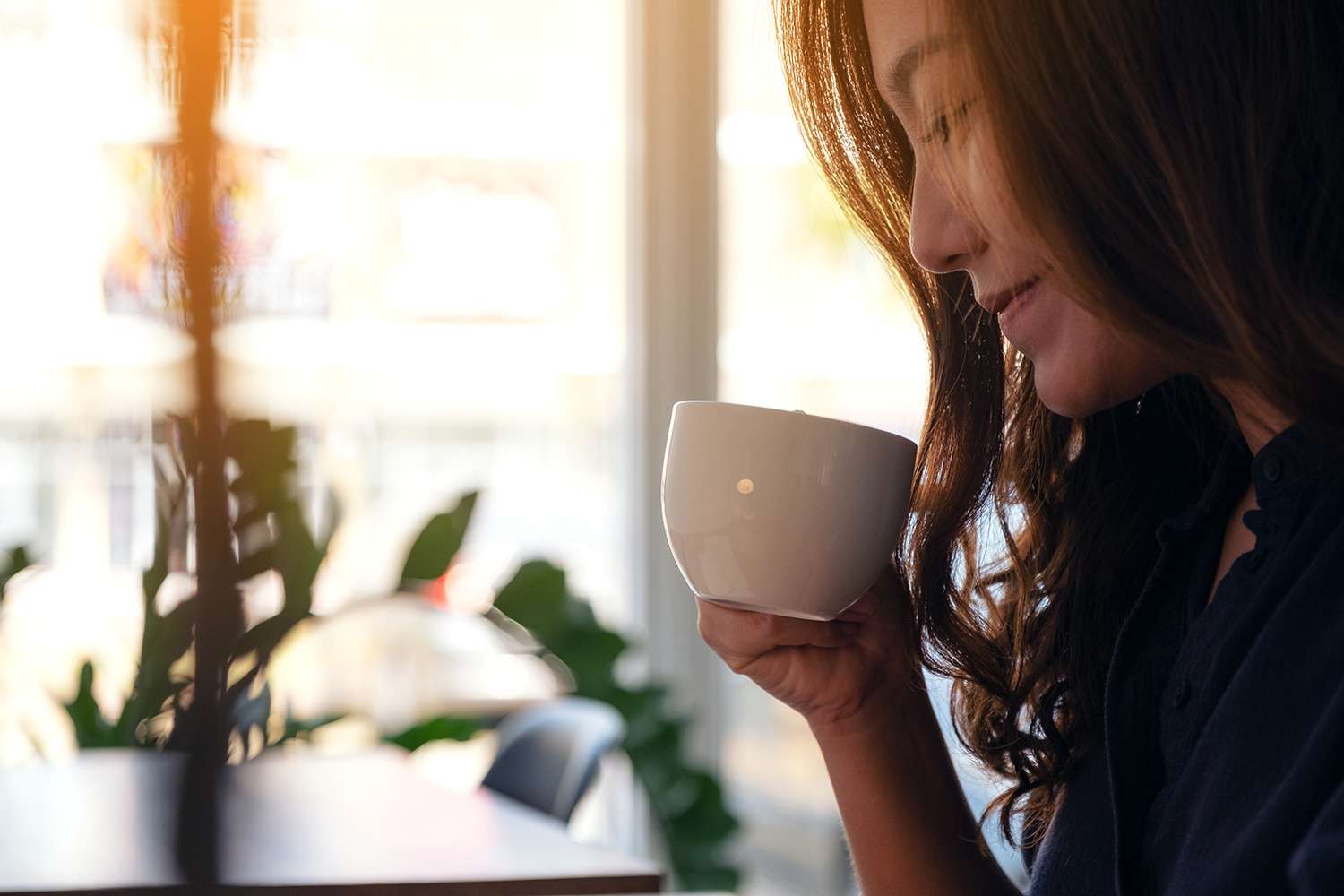 An image of a woman drinking from a mug and smiling from a blog post on the benefits of using a continuous glucose monitor.